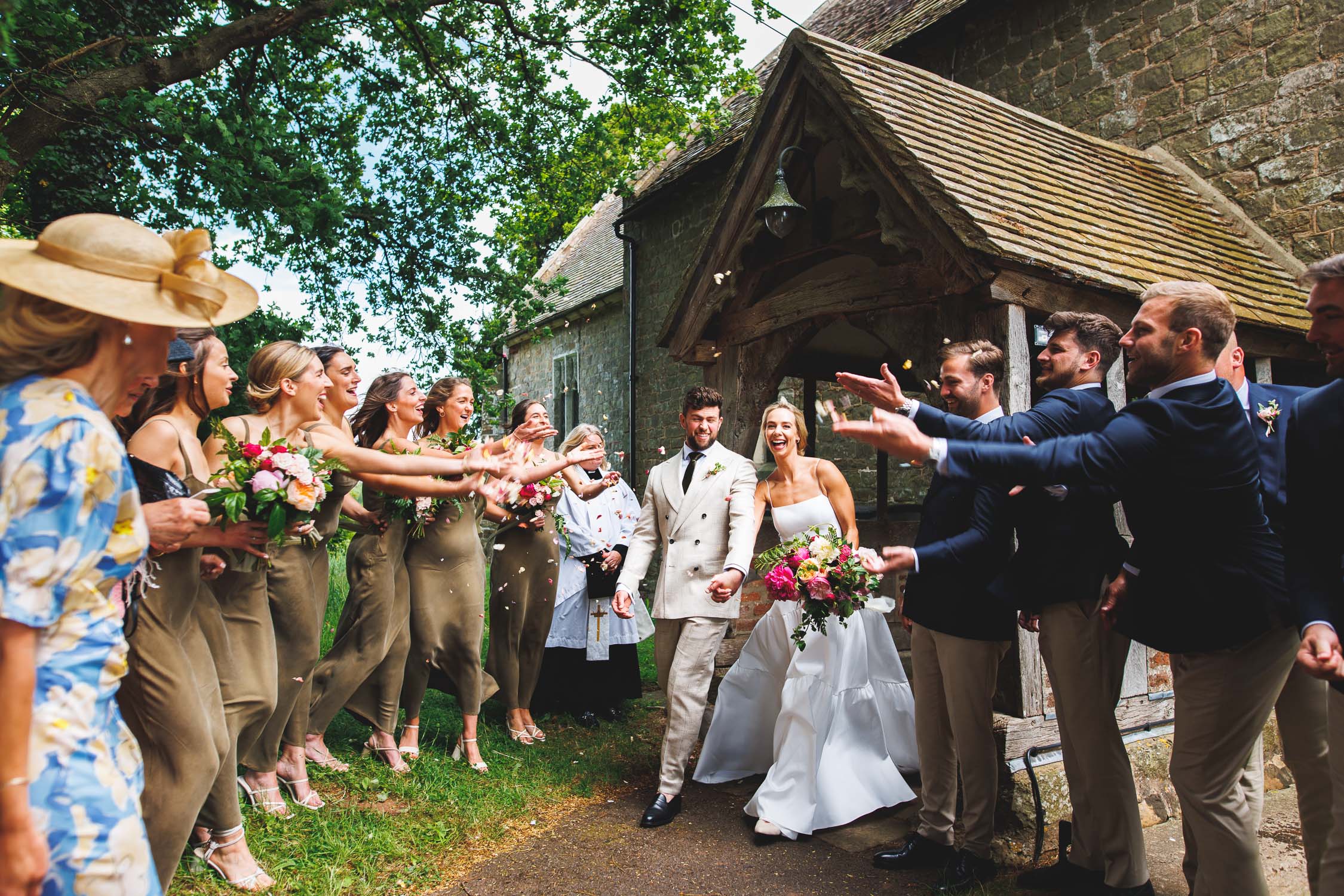 The Bride and Groom walk through a confetti tunnel made of their bridal party. Photographed at Pauntley Court.