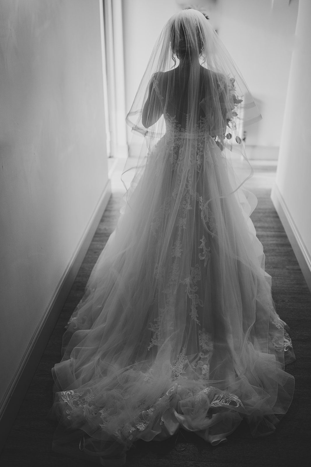 The bride walking away down the corridor, her train behind her, in black and white